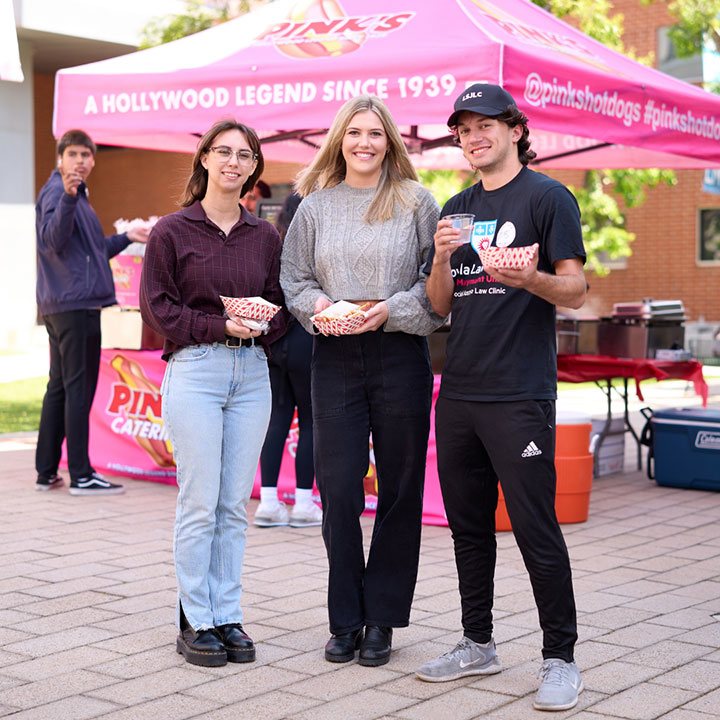 Three students standing in front of a hot dog stall with food