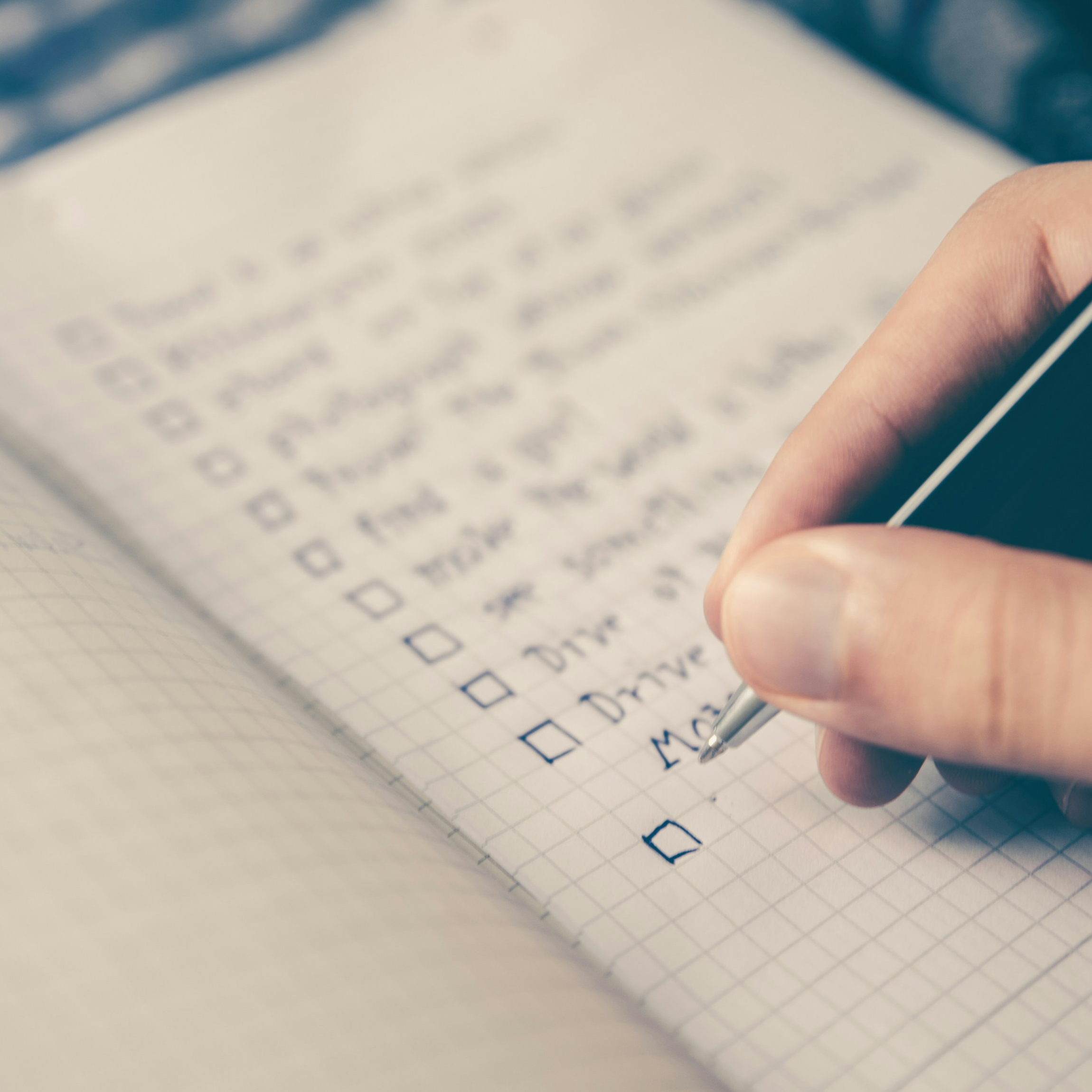 Open notebook with a checklist on the page and a hand writing on it.