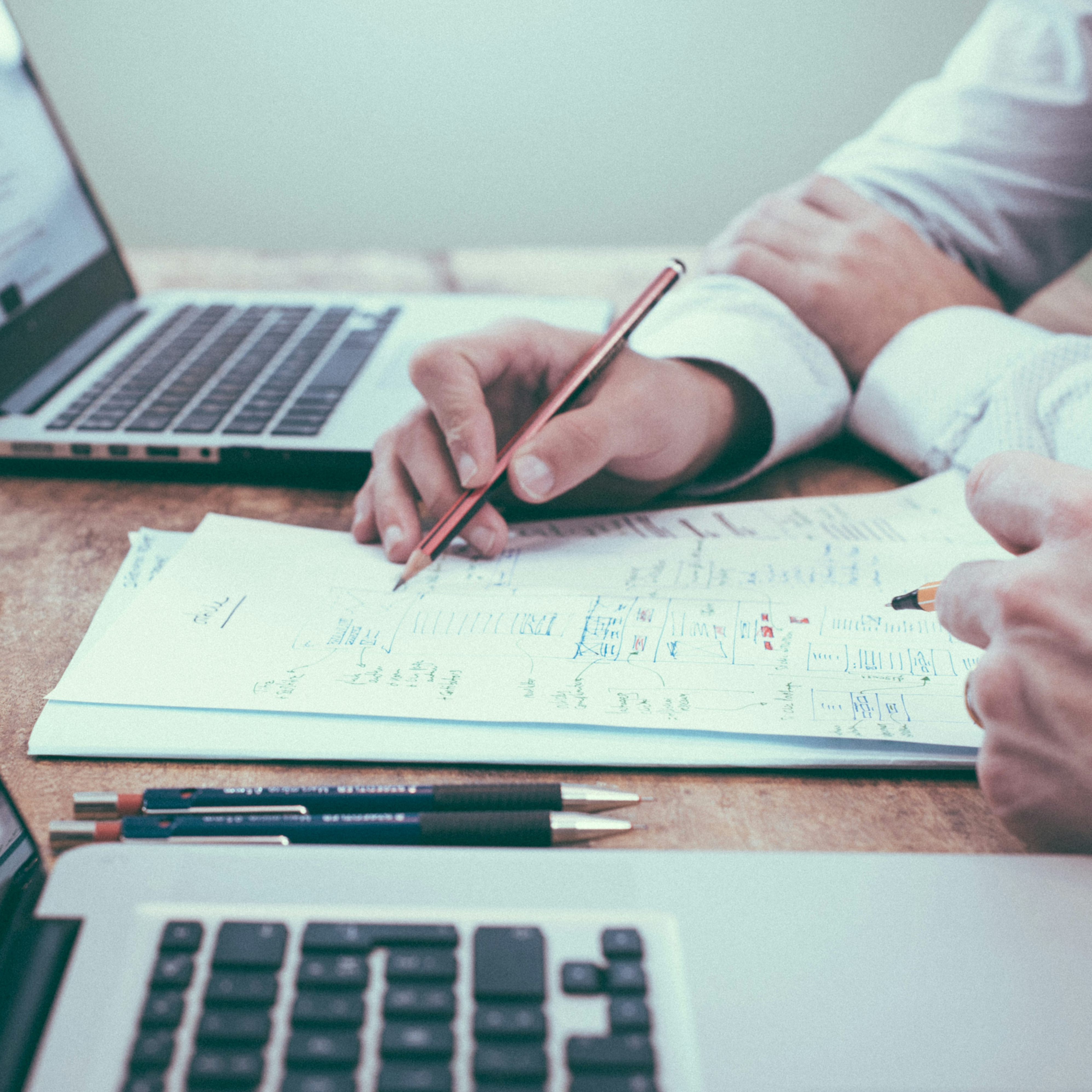 Two people at with laptops and a document between them